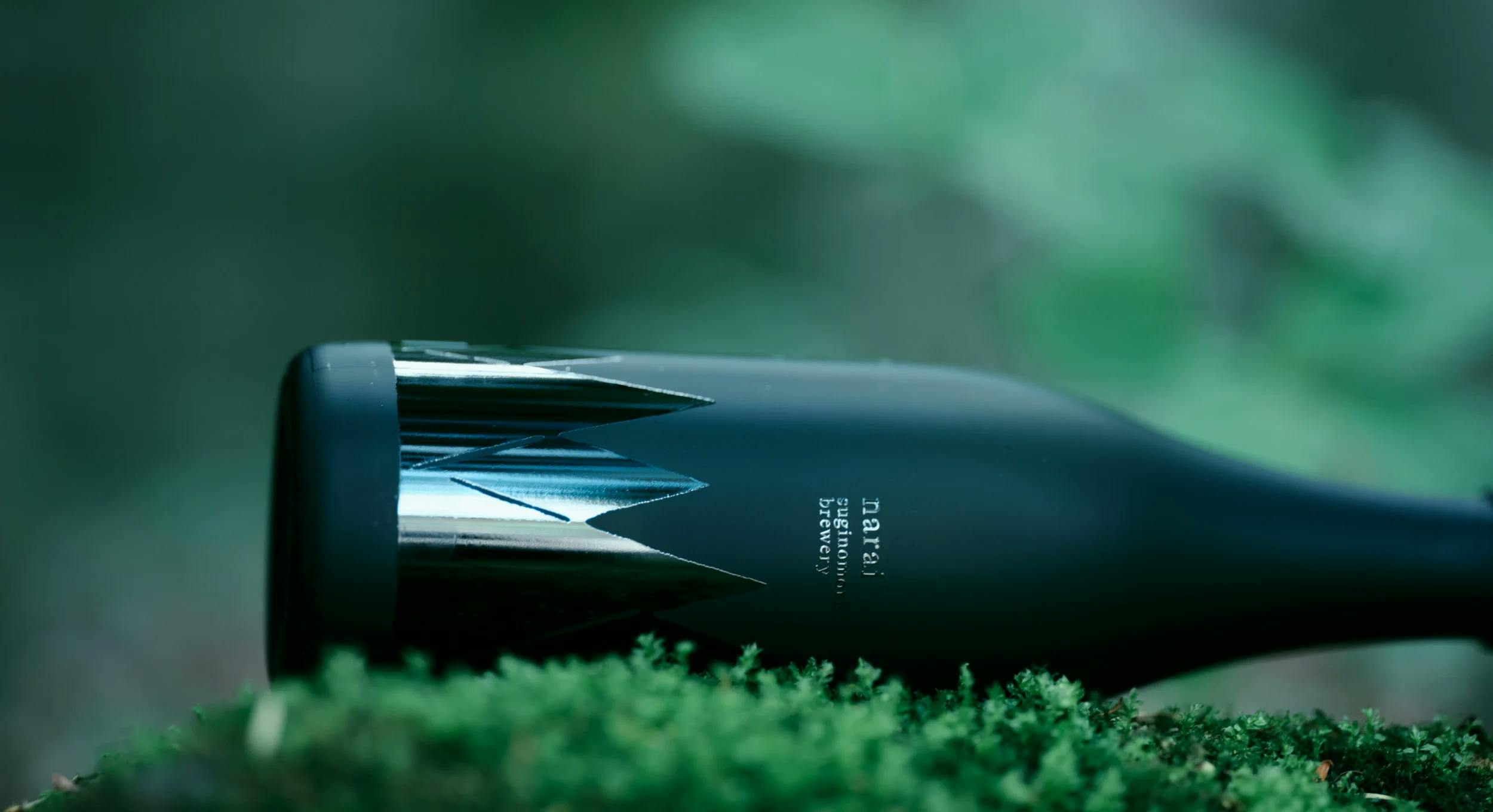 A picture of the Narai Black bottle resting on a mossy forest floor.