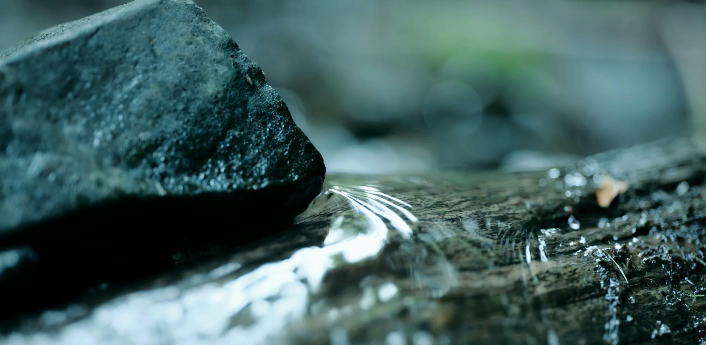 A picture of mountain stream water on a log, next to a rock.